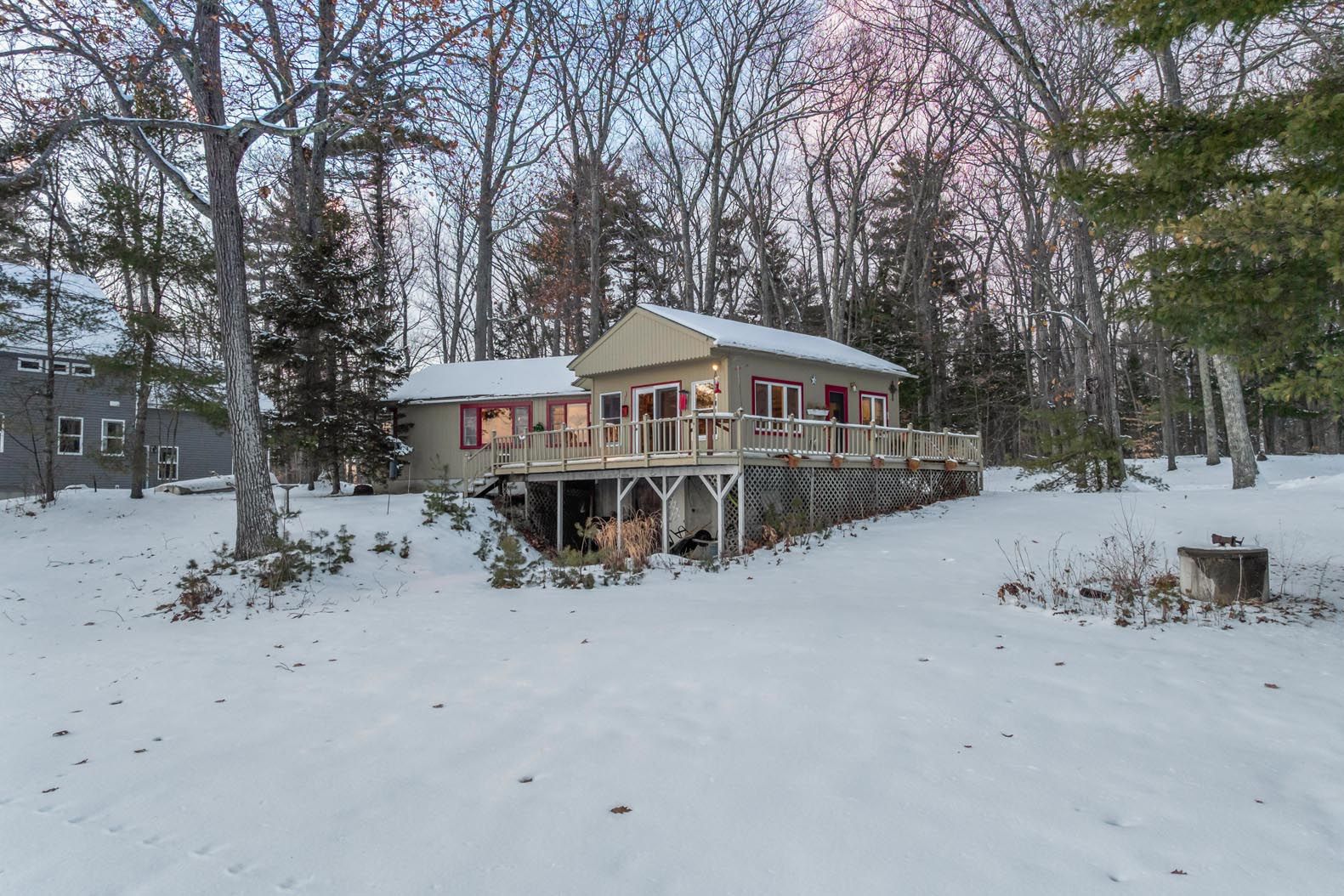 A cozy house surrounded by tall green trees and a well-maintained grassy lawn on a sunny day.