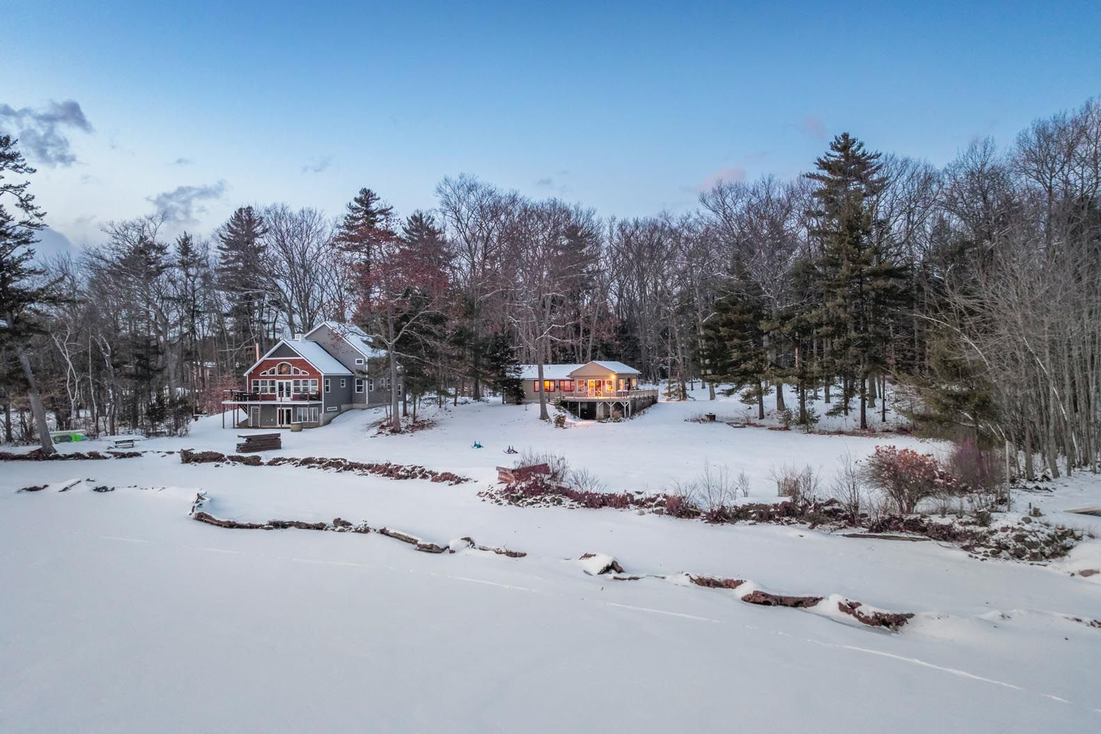 Aerial view of a lake with boats anchored near the shore, surrounded by lush green trees and distant mountains under a clear blue sky.