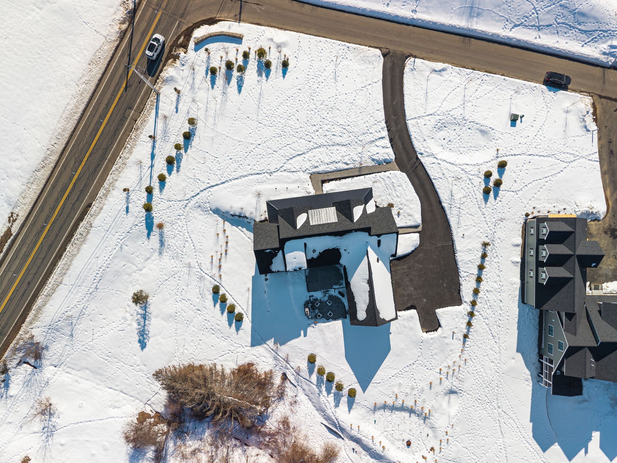 Modern blue house with stone accents, large windows, and a three-car garage, surrounded by snow and leafless trees in winter.