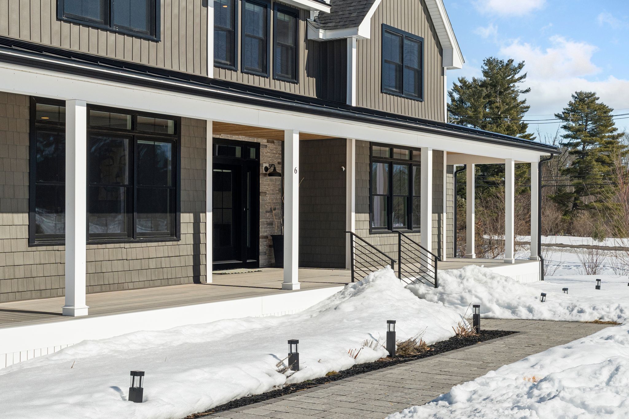 Modern black house with large windows, snow-covered front yard, surrounded by trees, in winter season, aerial view.