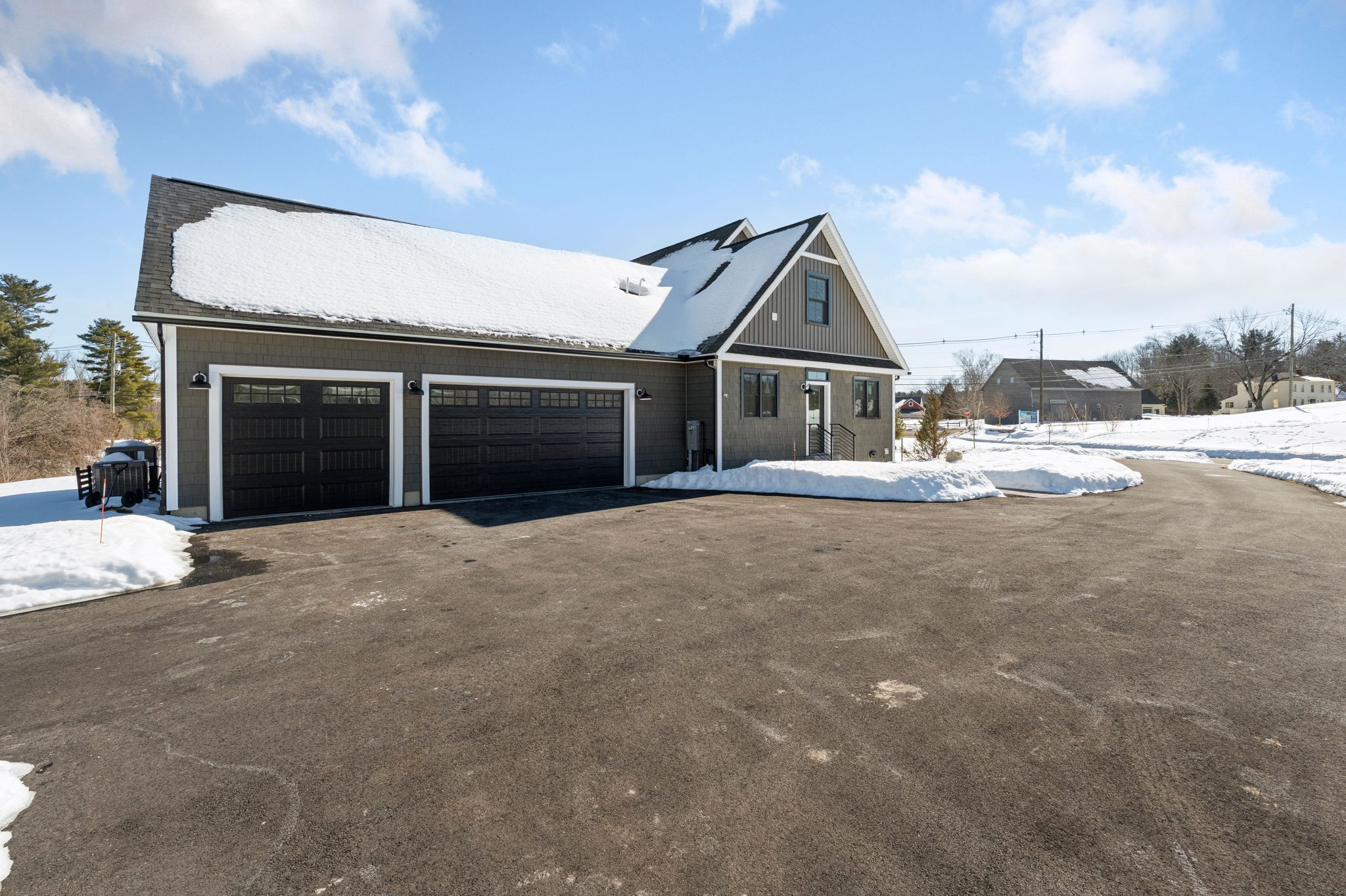 Modern gray and black two-story house with stone accents on foundation surrounded by snow and trees in winter.