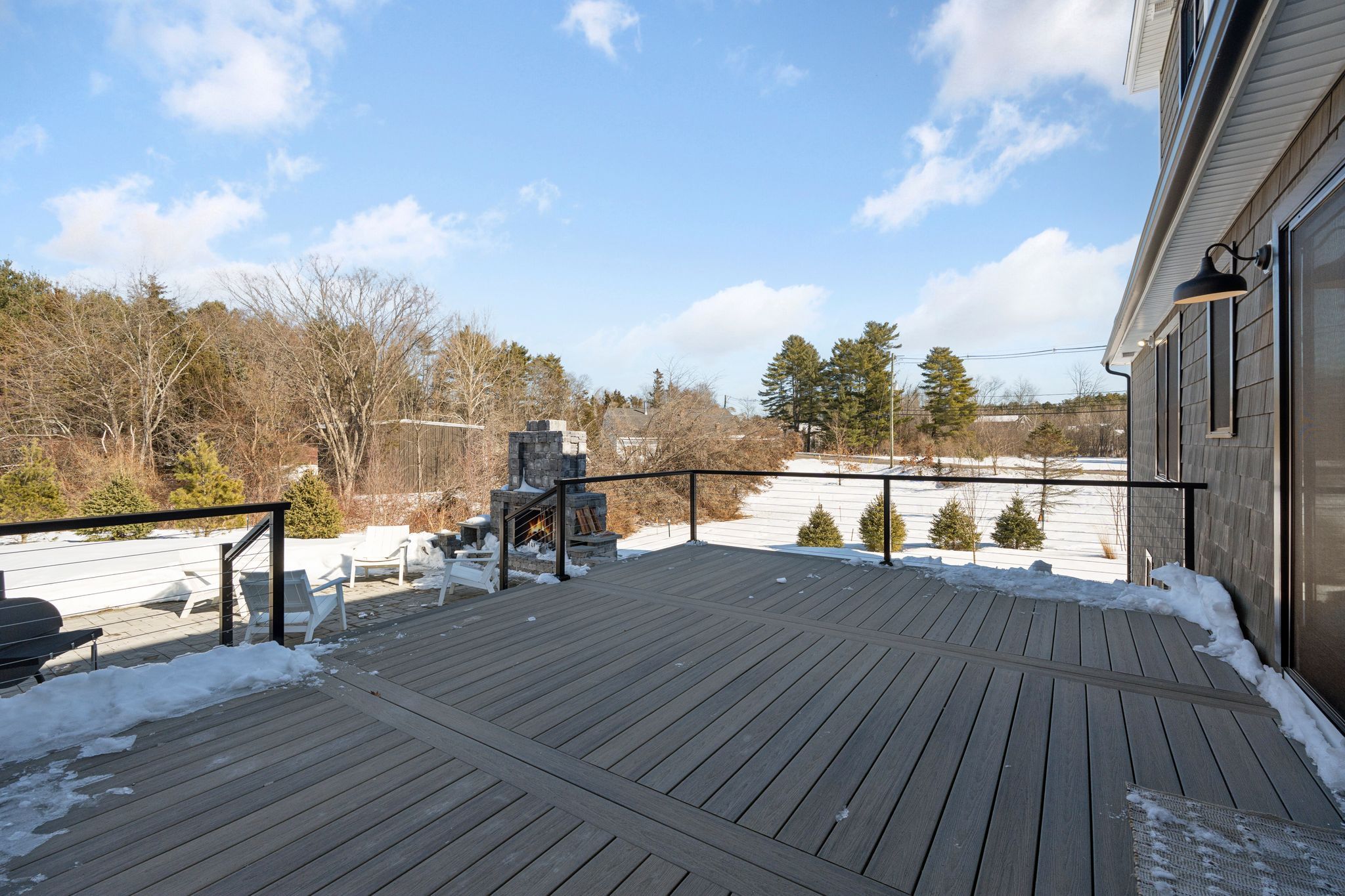 Spacious dark gray two-story house with warm yellow interior lighting, surrounded by snow-covered yard during winter sunset, with leafless trees in the background.