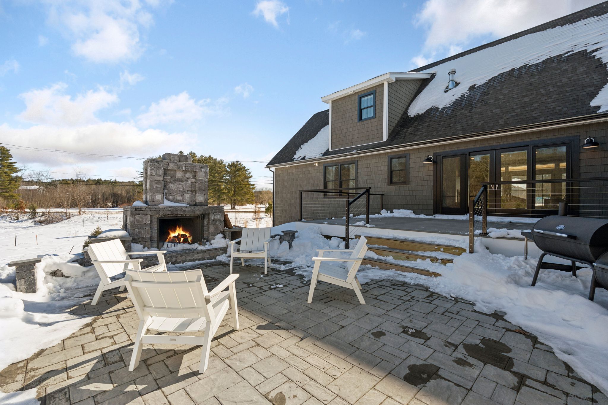 Modern black house with a stone foundation and snow-covered landscape during sunset