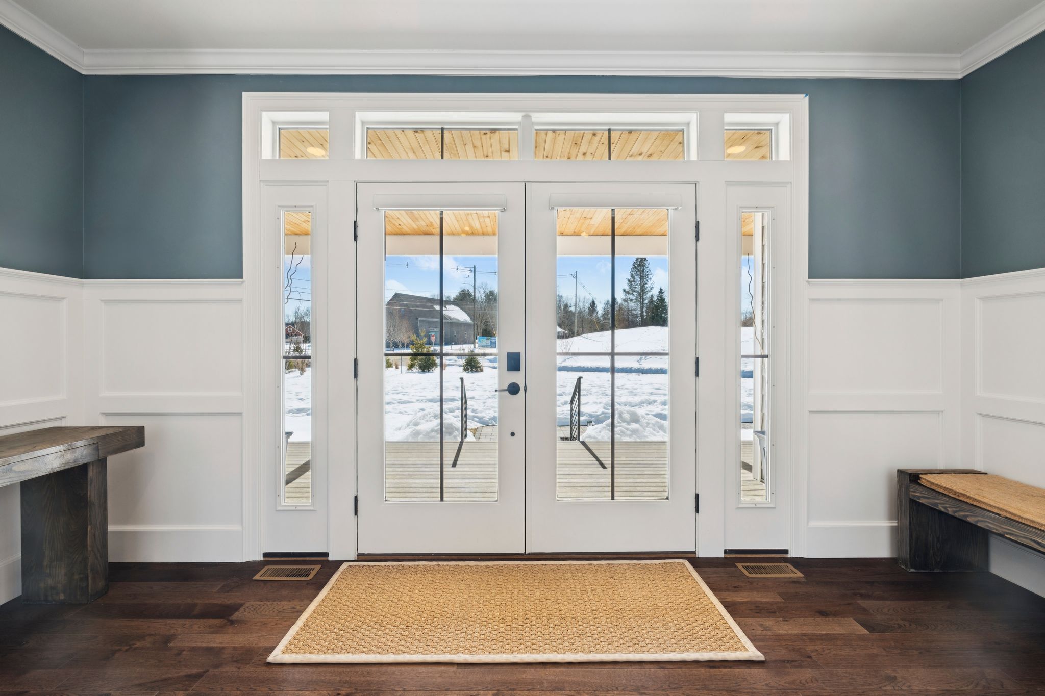 Aerial view of a snow-covered residential neighborhood near a large blue lake with a bridge crossing over the water, surrounded by trees and mountains in the distance.