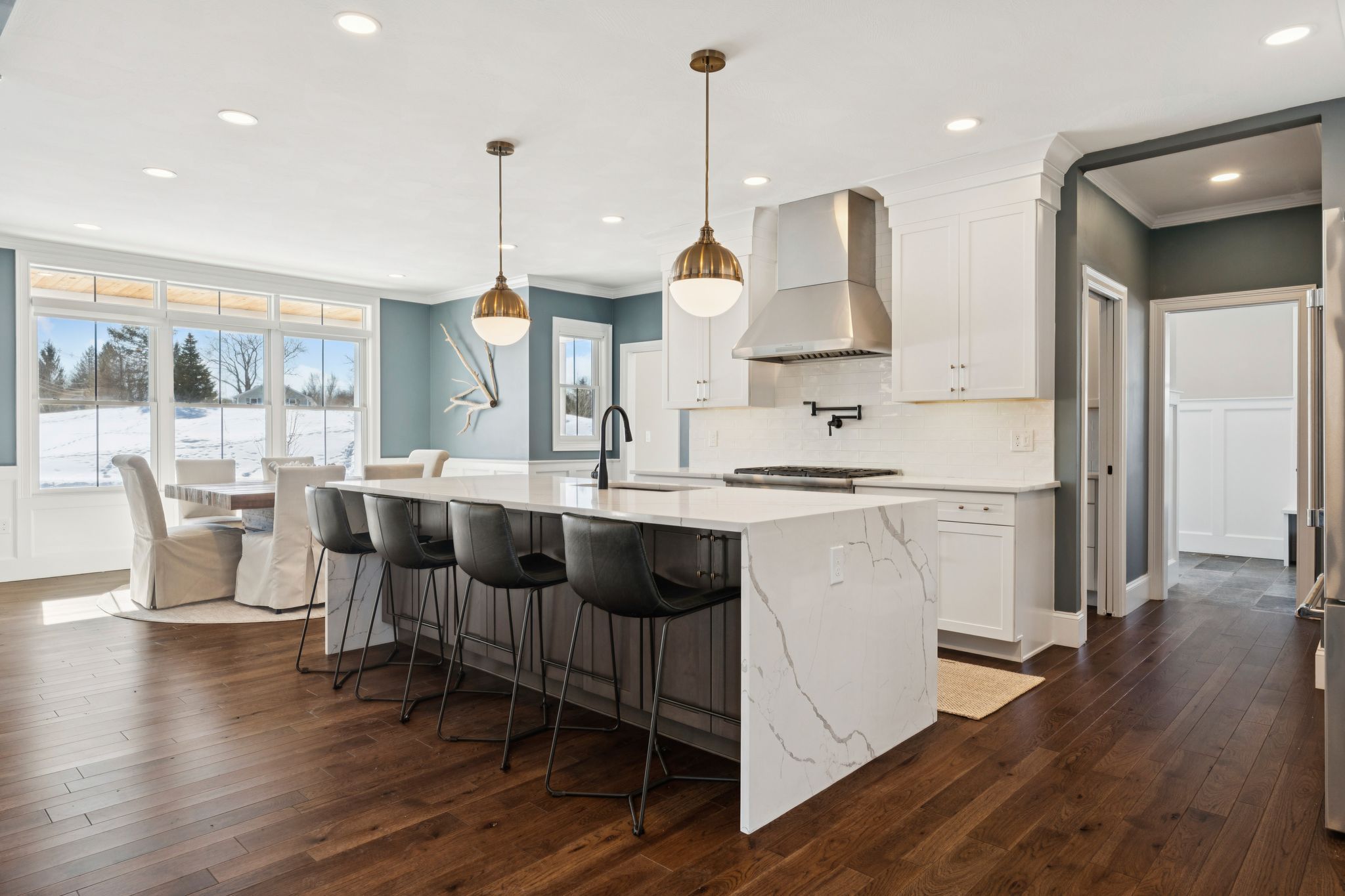 Aerial view of a snow-covered house surrounded by leafless trees and a winding driveway on a winter day