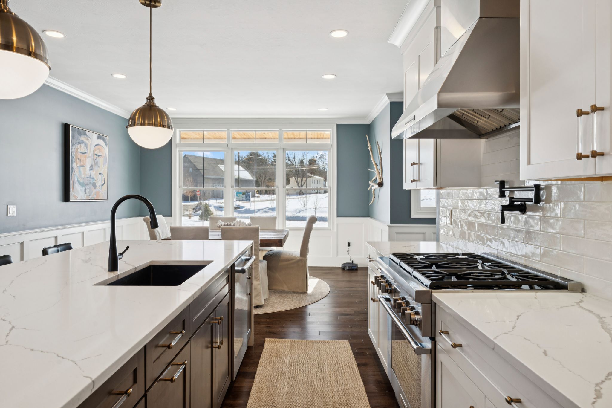 Modern black house with large windows, snow-covered front yard, surrounded by trees, in winter season, aerial view.