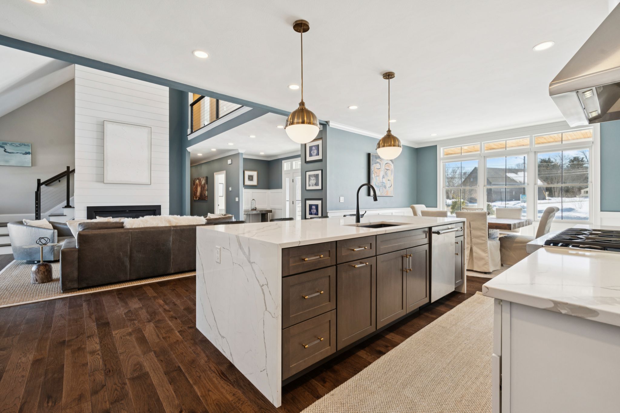 Modern gray and black two-story house with stone accents on foundation surrounded by snow and trees in winter.