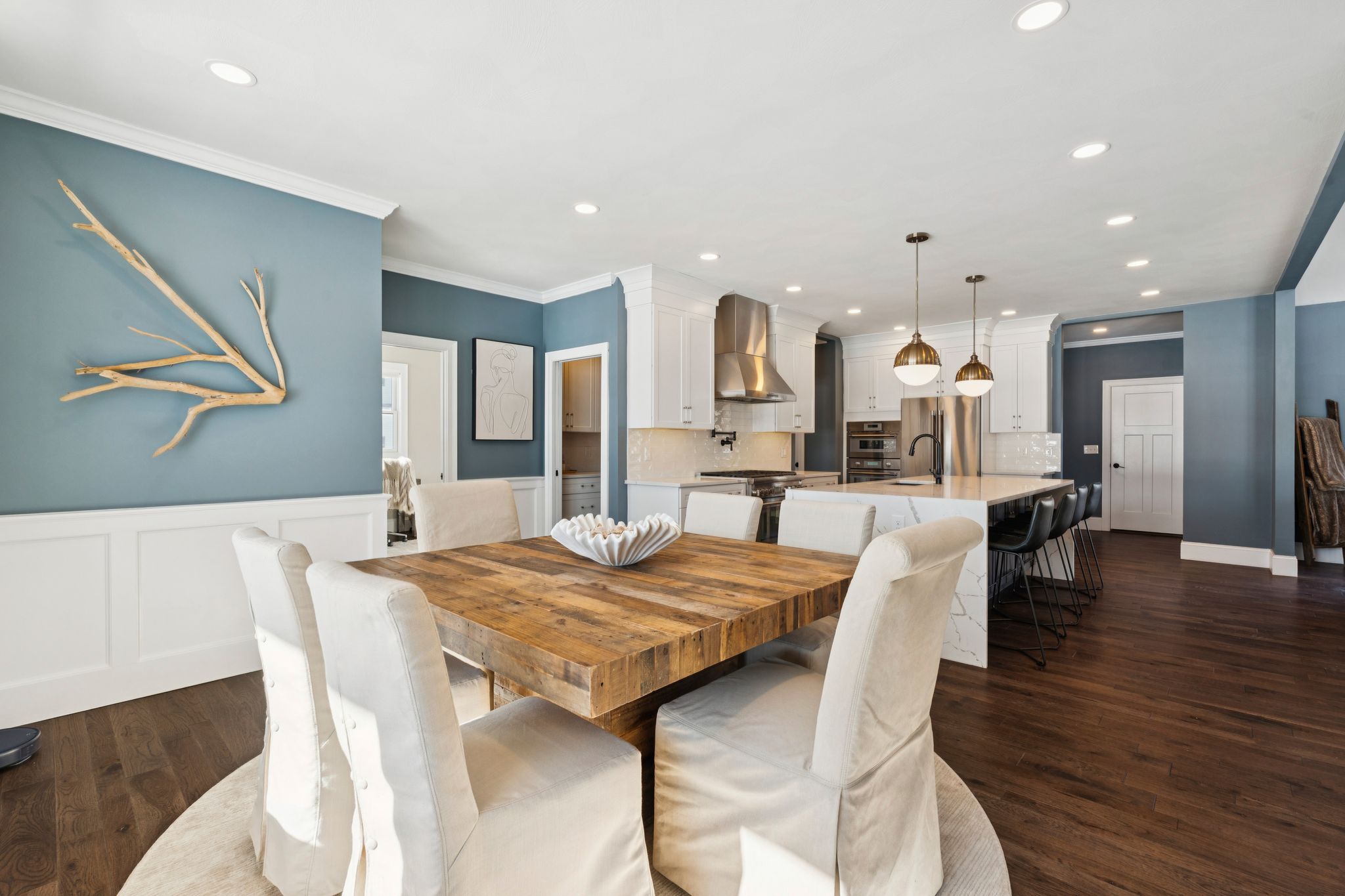 Spacious dark gray two-story house with warm yellow interior lighting, surrounded by snow-covered yard during winter sunset, with leafless trees in the background.