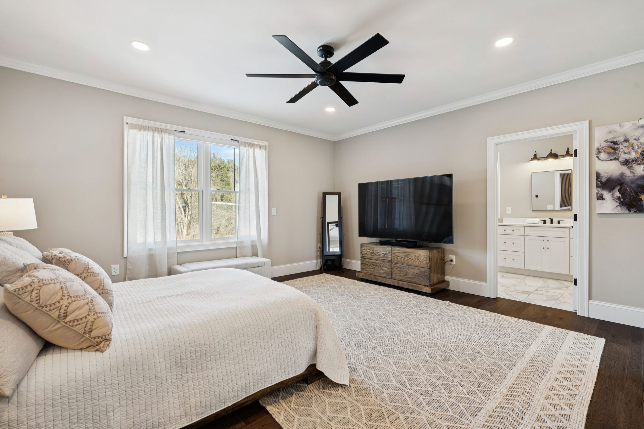 Modern contemporary house with large windows, stone and gray siding, surrounded by snow, located near a wooded area during sunset.