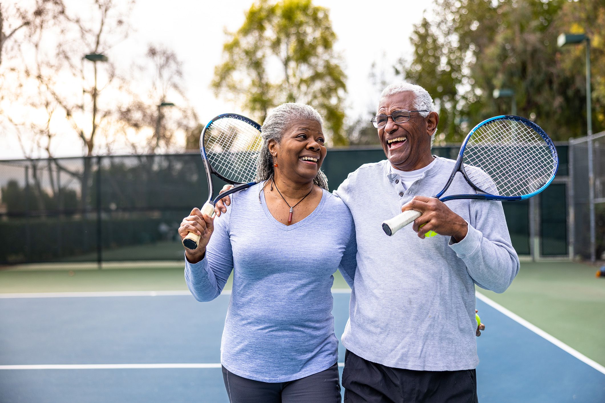 Happy elderly couple playing tennis together on outdoor court, smiling and enjoying active lifestyle, representing senior fitness and recreation.