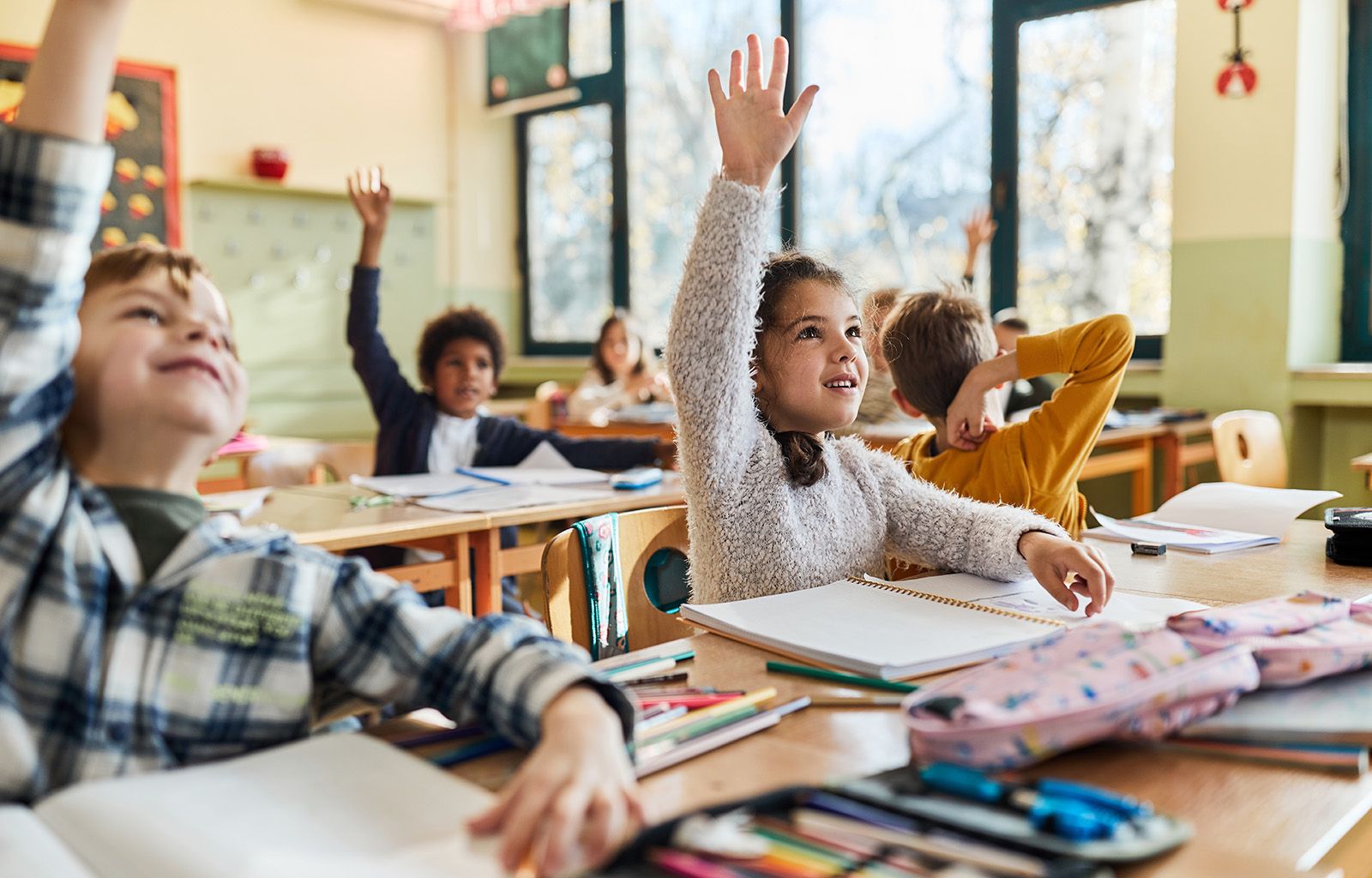 Elementary school students raising their hands in a classroom during a lesson.