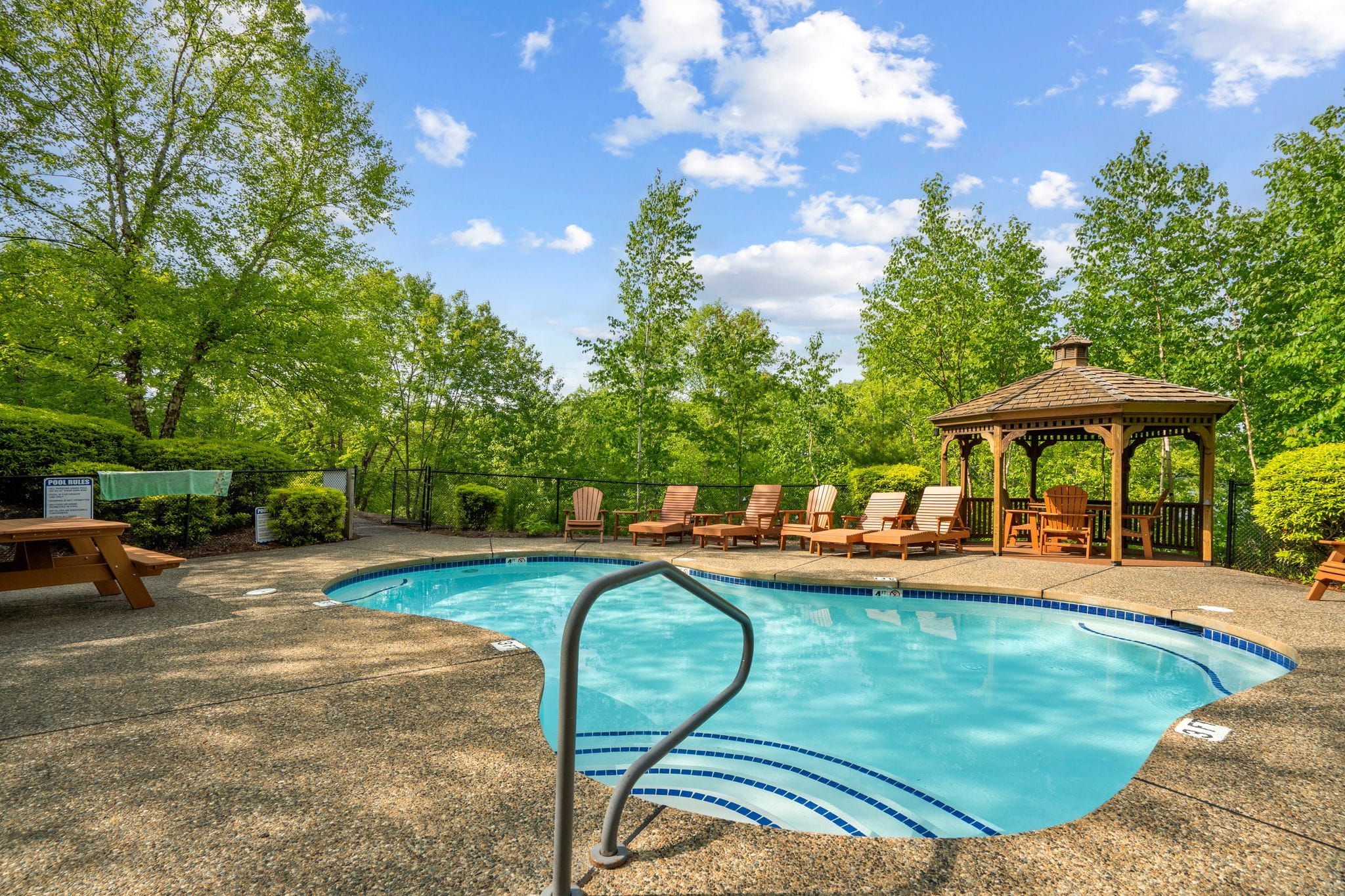 Cozy bedroom with king-sized bed, dark gray bedding, white pillows, wooden nightstands with lamps, wall-mounted mountain artwork, window with lush green trees outside, and rustic wooden ski patrol sign.