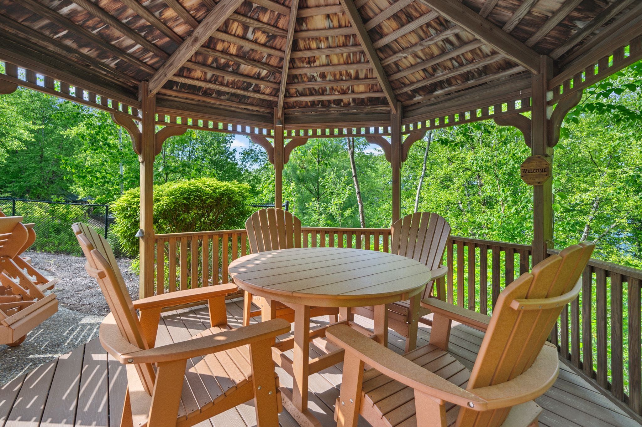 Bright bedroom with large arched window overlooking a green outdoor landscape, featuring a bed with cream-colored bedding, a wooden dresser with a vase of flowers, and a decorative mirror on a gray wall.