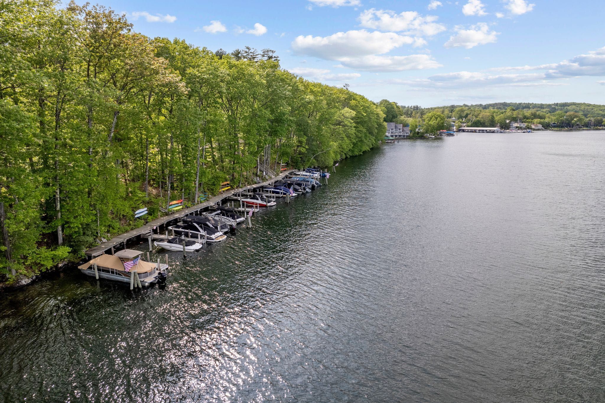 Modern kitchen with blue island and barstools, wooden cabinetry, mosaic backsplash, and large windows letting in natural light, decorated with flowers and seaside artwork.