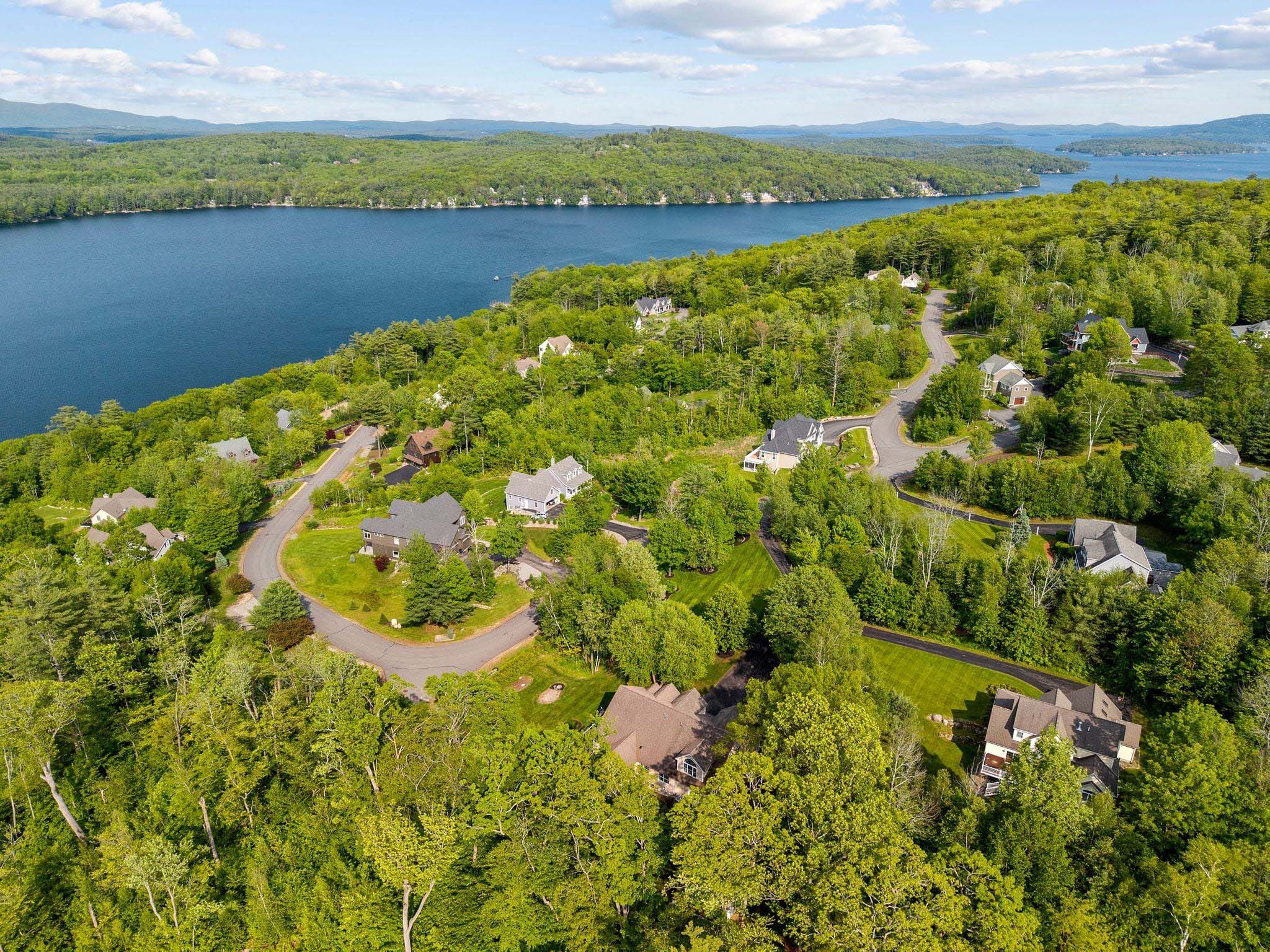 Modern kitchen with beige wooden cabinets, stainless steel appliances, mosaic tile backsplash, blue kitchen island with barstools, and large window with view of green trees.