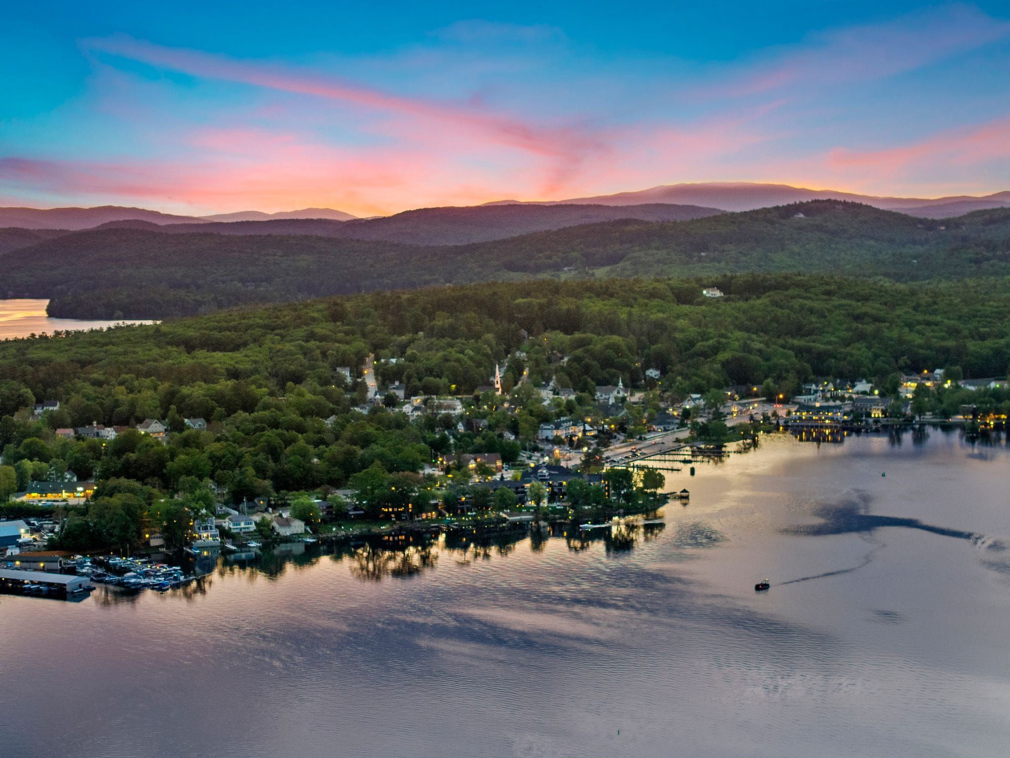 Bright and spacious modern kitchen with a large island, blue upholstered bar stools, stainless steel appliances, wooden cabinets, and large windows letting in natural light.