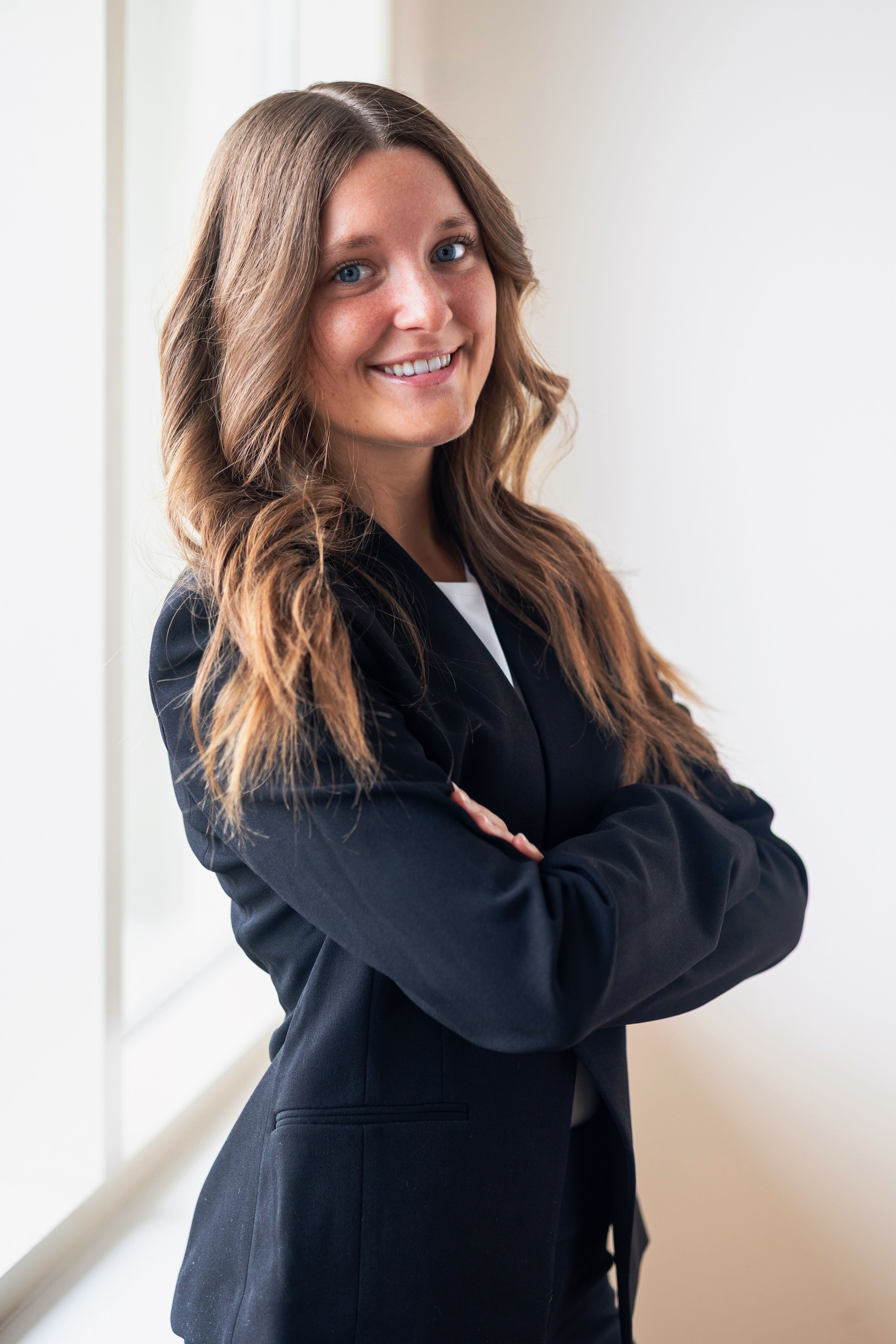 Smiling woman with brown hair in a black blazer with arms crossed.