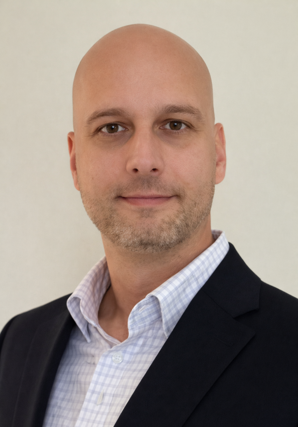 A bald, smiling man wearing a black suit top over a white and gray tattersall patterned polo.