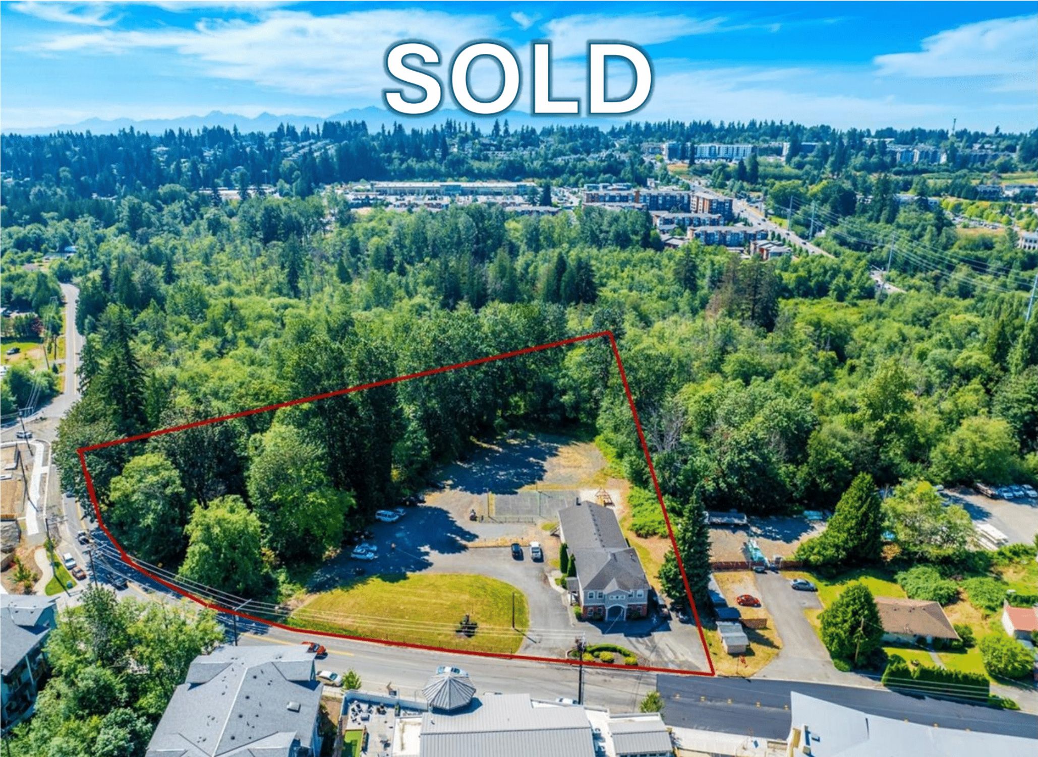 Aerial view of a cleared residential property with a house, surrounded by a wooded area, outlined in red, with a 