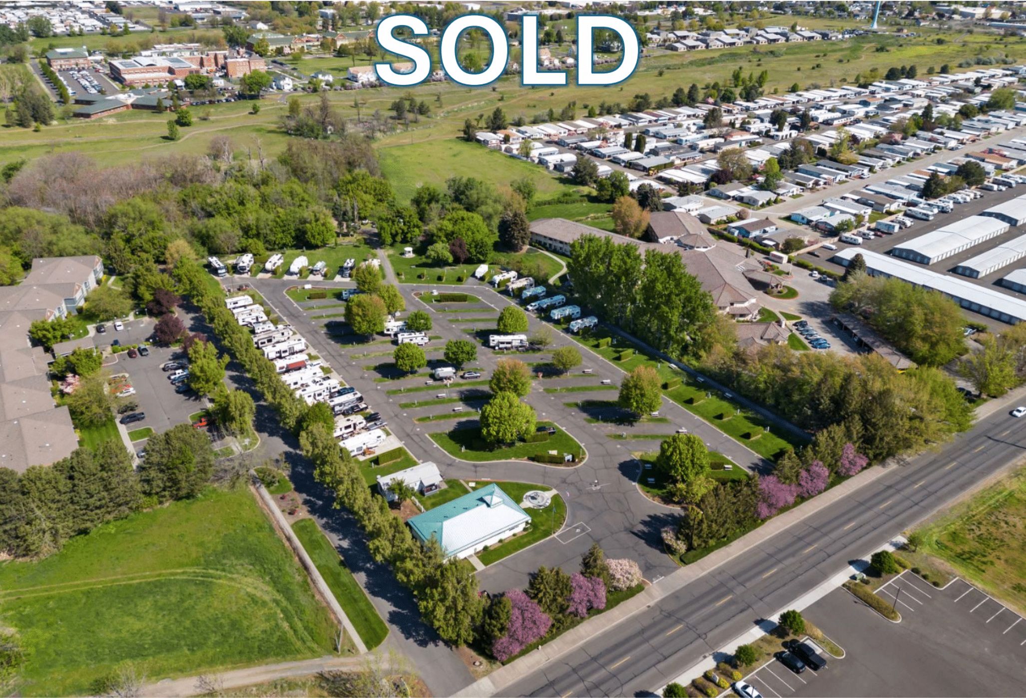 Aerial view of a large parking lot with numerous parked vehicles, surrounded by trees and greenery, with a 