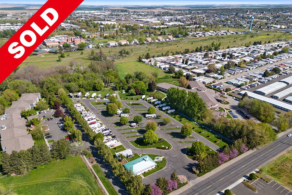 Aerial view of a large parking lot with numerous parked vehicles, surrounded by trees and greenery, with a 