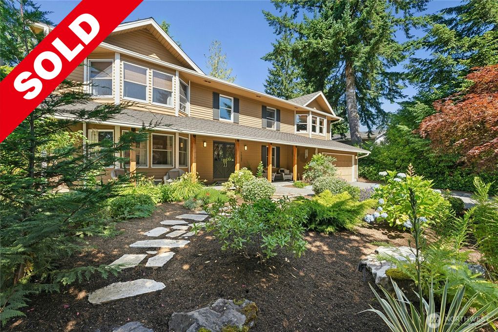 Beautiful two-story house with a well-maintained front yard featuring lush greenery and flower beds, sold property under blue sky.