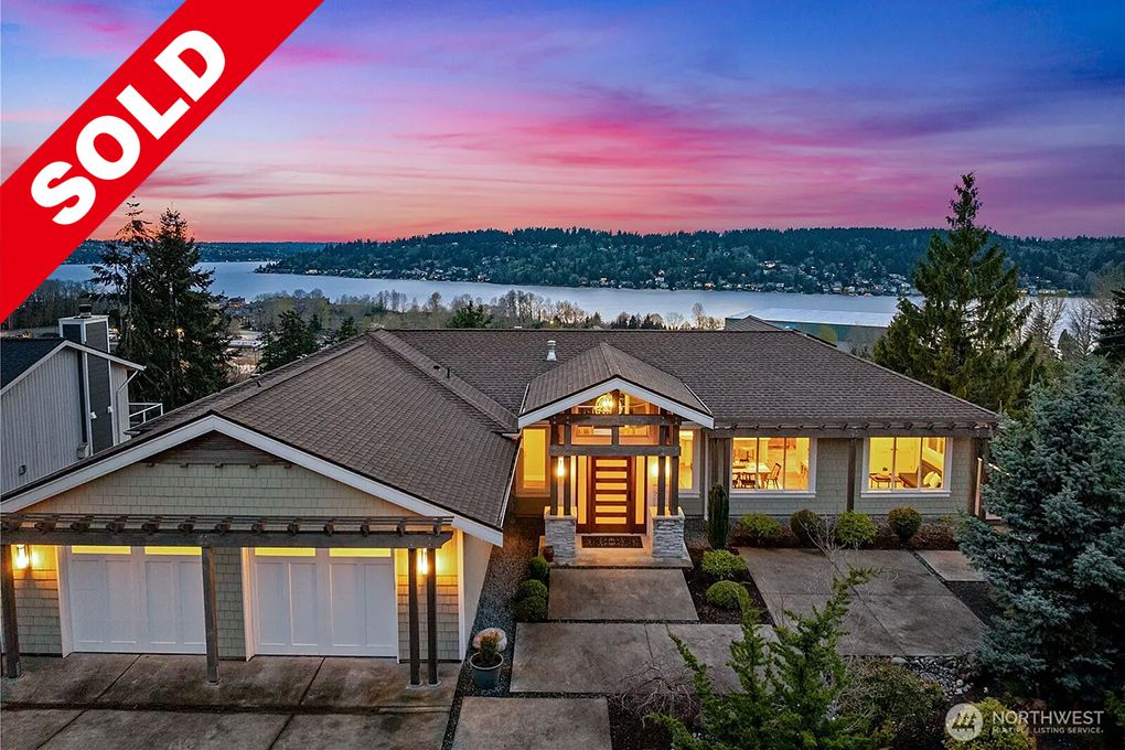 Sold sign on a modern house with large windows overlooking a scenic lake and sunset sky.