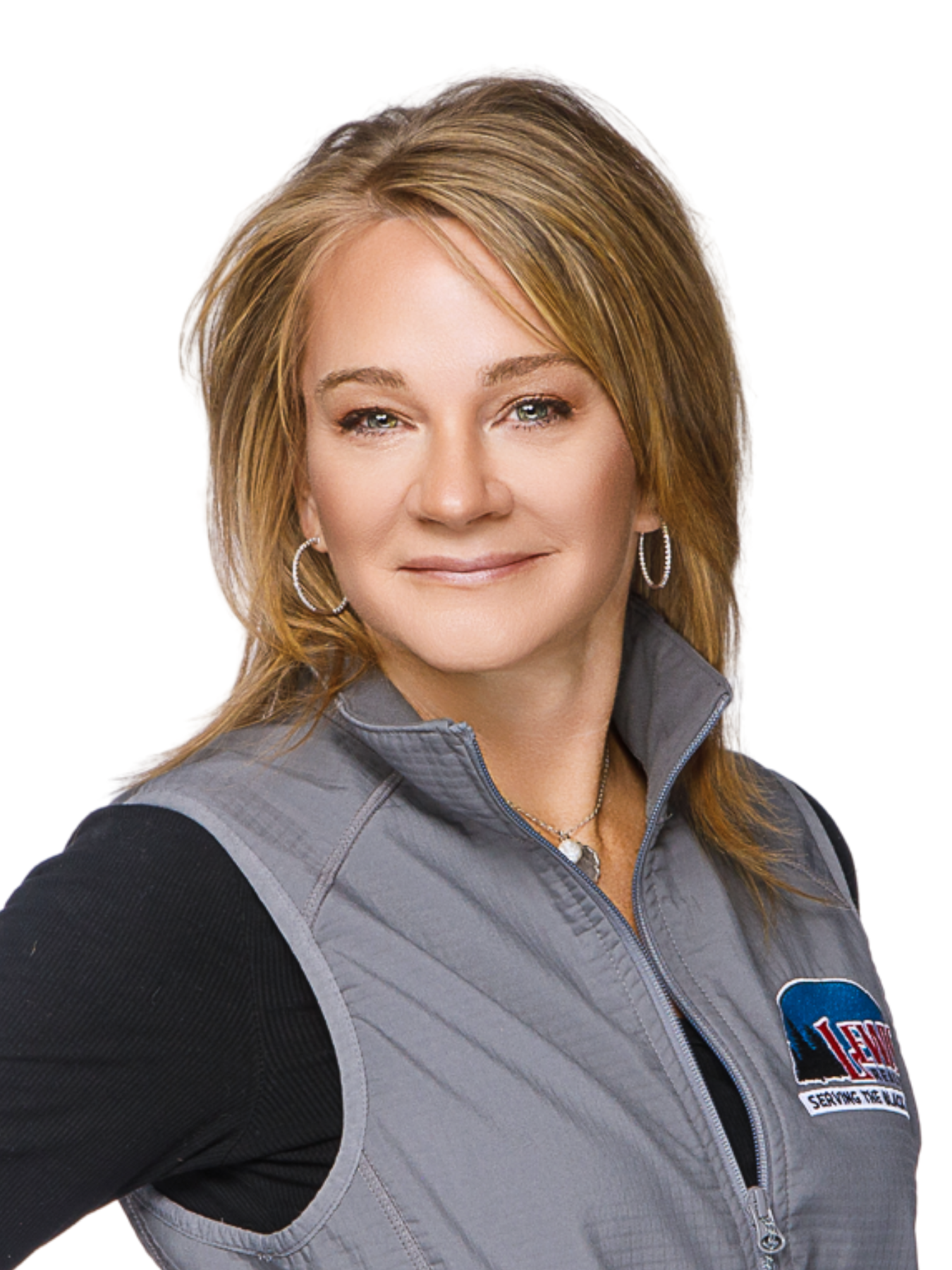 Portrait of a confident woman with red hair, smiling with arms crossed, wearing a black and gray jacket with a logo on the chest, against a white background.
