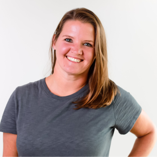Smiling woman with shoulder-length light brown hair wearing a casual grey t-shirt against a plain white background.