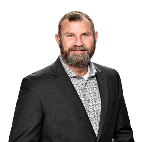 Professional portrait of a middle-aged man with a beard wearing a dark suit and checkered shirt, smiling against a white background.