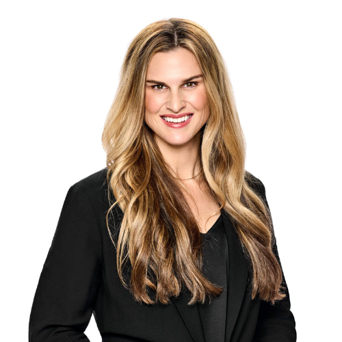 Professional woman with long wavy blonde hair, wearing a black blazer and smiling confidently against a white background.