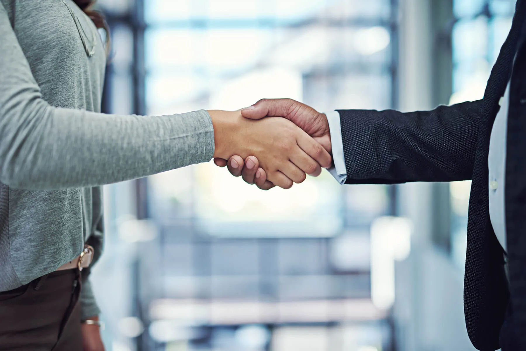Handshake between a woman in casual attire and a man in a formal suit, symbolizing a professional business agreement or partnership.