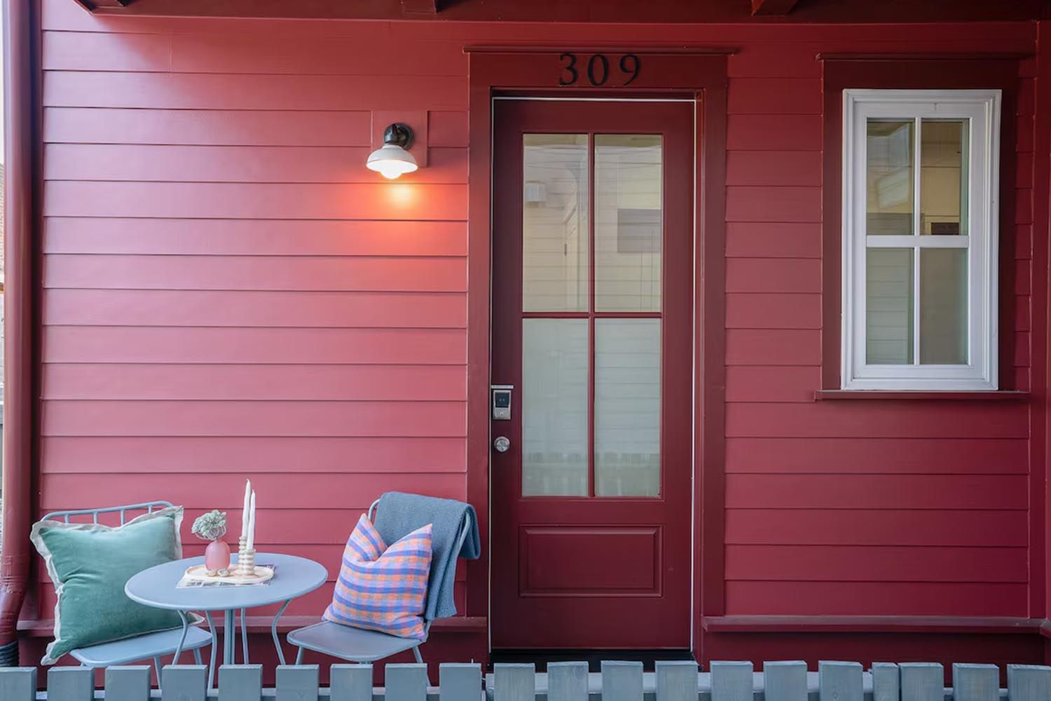 Bright and modern living room with beige sofas, colorful throw pillows, wooden coffee table, black and leather accent chairs, large window with orange curtains, hardwood floors, and decorative wall art.