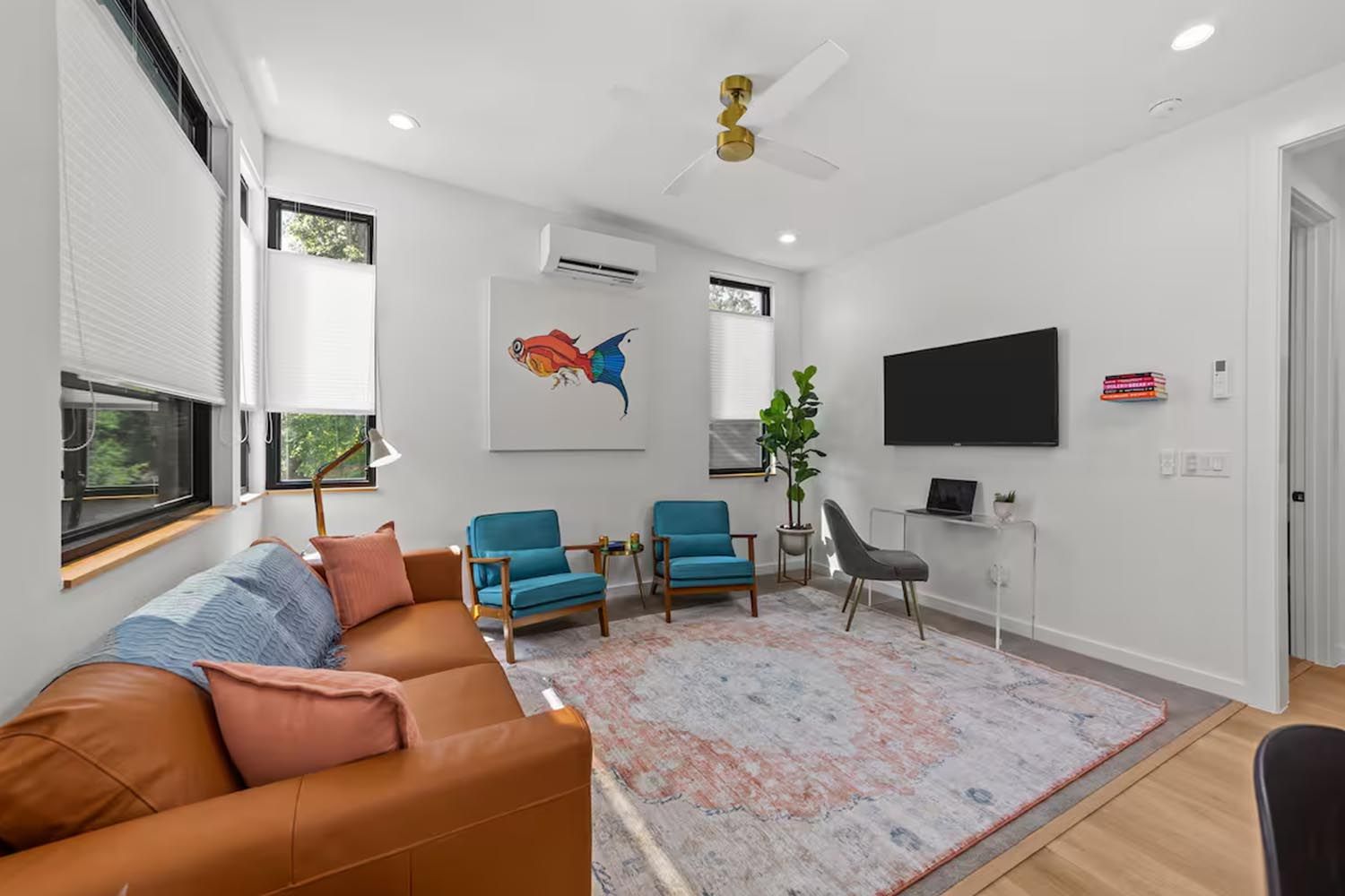 Bright and modern living room with beige sofas, colorful throw pillows, wooden coffee table, black and leather accent chairs, large window with orange curtains, hardwood floors, and decorative wall art.