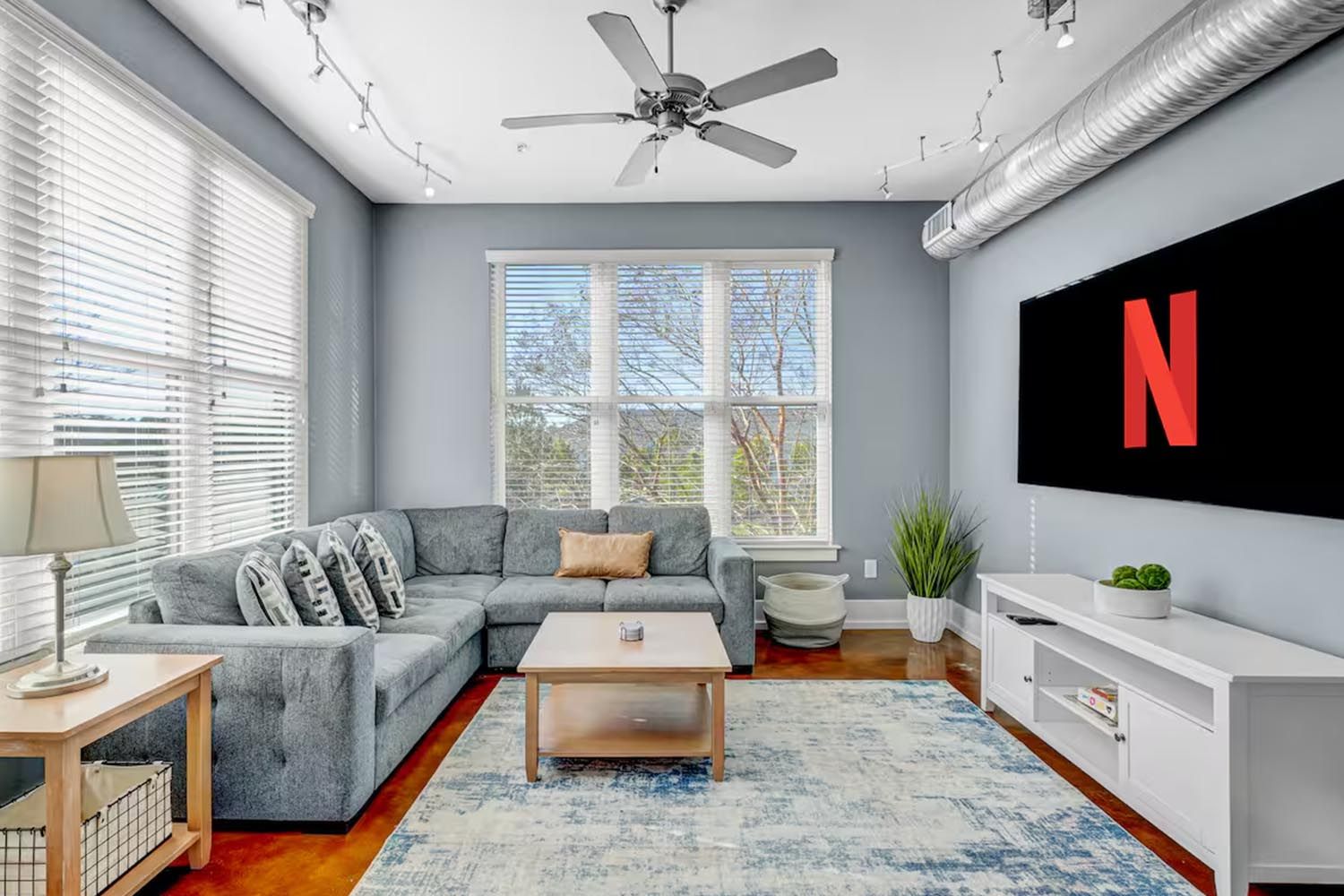 Bright and modern living room with beige sofas, colorful throw pillows, wooden coffee table, black and leather accent chairs, large window with orange curtains, hardwood floors, and decorative wall art.