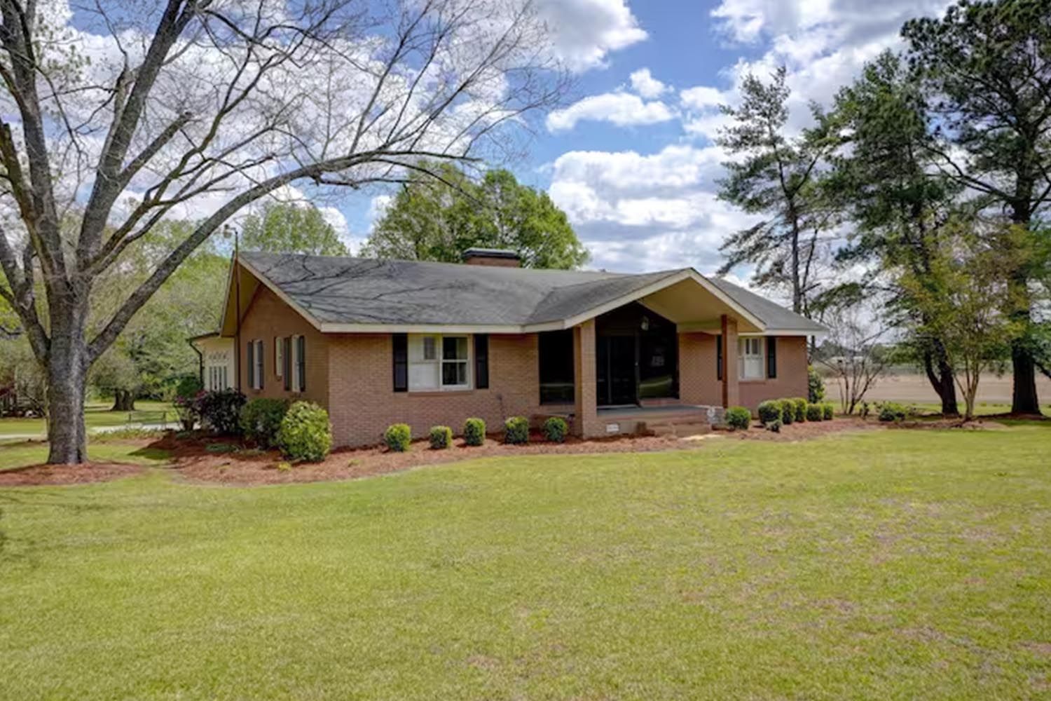 Bright and modern living room with beige sofas, colorful throw pillows, wooden coffee table, black and leather accent chairs, large window with orange curtains, hardwood floors, and decorative wall art.