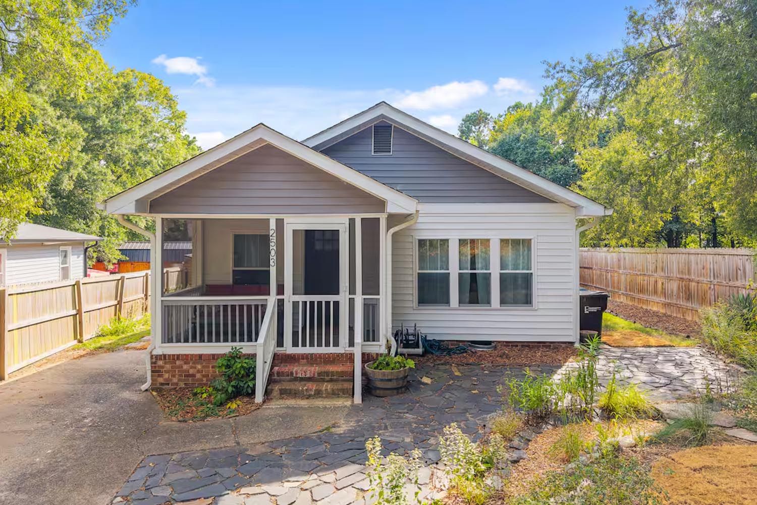 Bright and modern living room with beige sofas, colorful throw pillows, wooden coffee table, black and leather accent chairs, large window with orange curtains, hardwood floors, and decorative wall art.