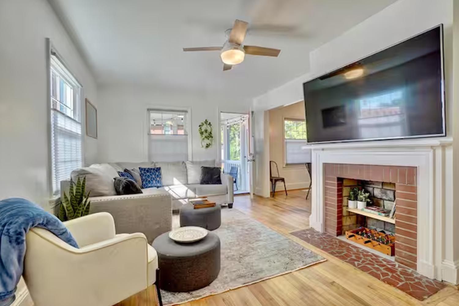 Bright and modern living room with beige sofas, colorful throw pillows, wooden coffee table, black and leather accent chairs, large window with orange curtains, hardwood floors, and decorative wall art.