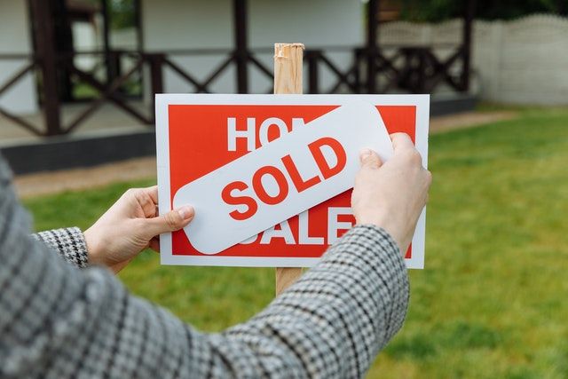 a sign of home for sale in front of a house beign covered by a sign of sold