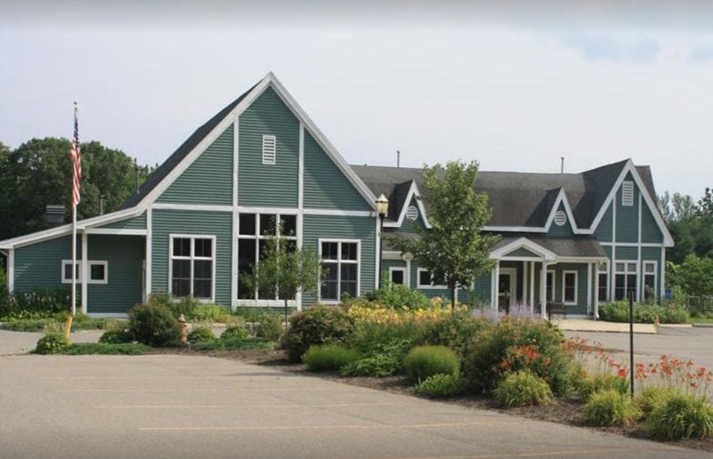 Modern blue residential house with large windows, landscaped garden, and parking lot in front