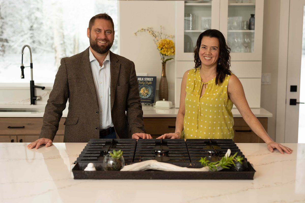 Smiling man and woman standing in a modern kitchen by a cooktop with plants and decorative elements.