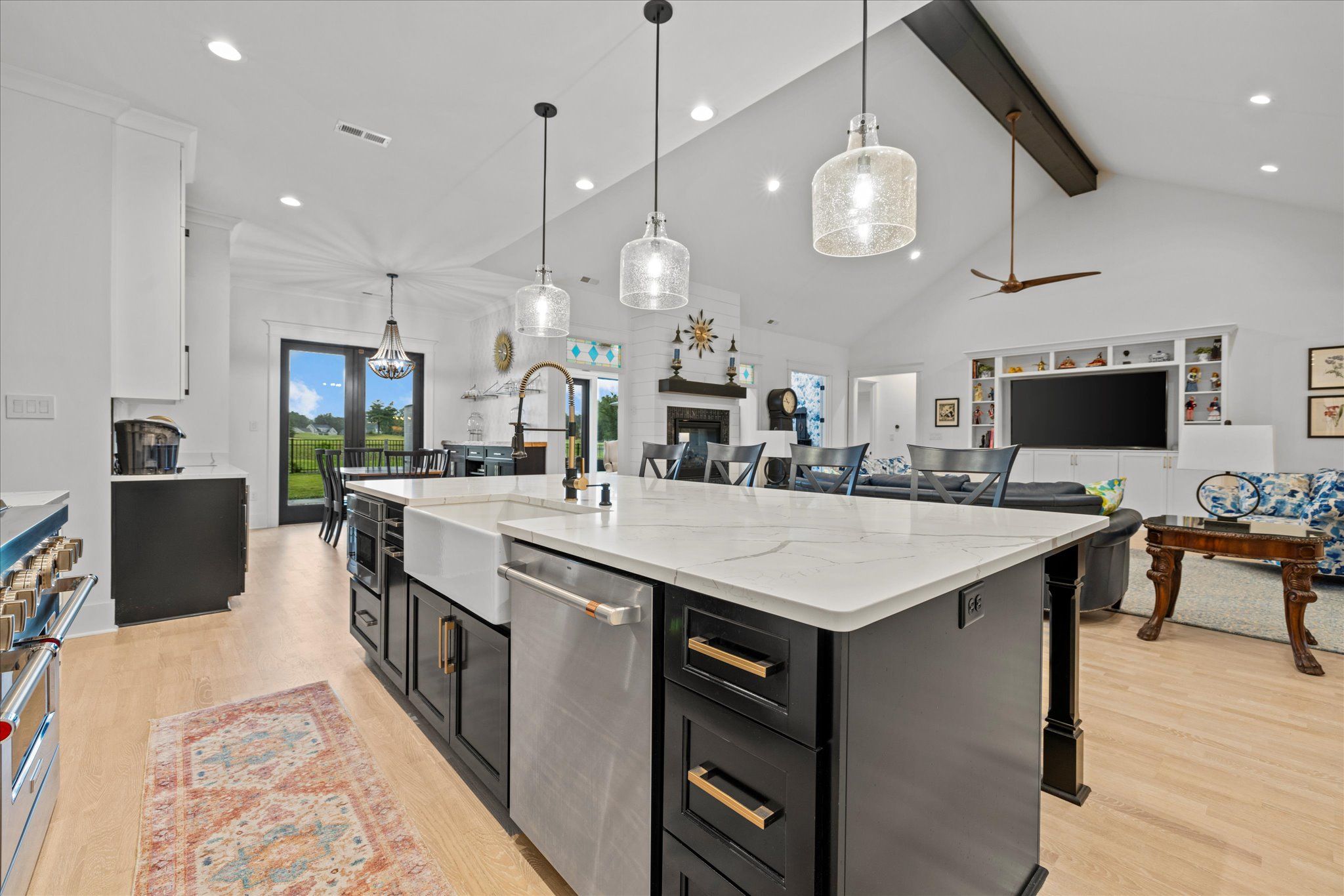 Modern open-concept kitchen and living room with white walls, black cabinetry, island with marble countertop, pendant lighting, and large glass doors leading to green backyard garden